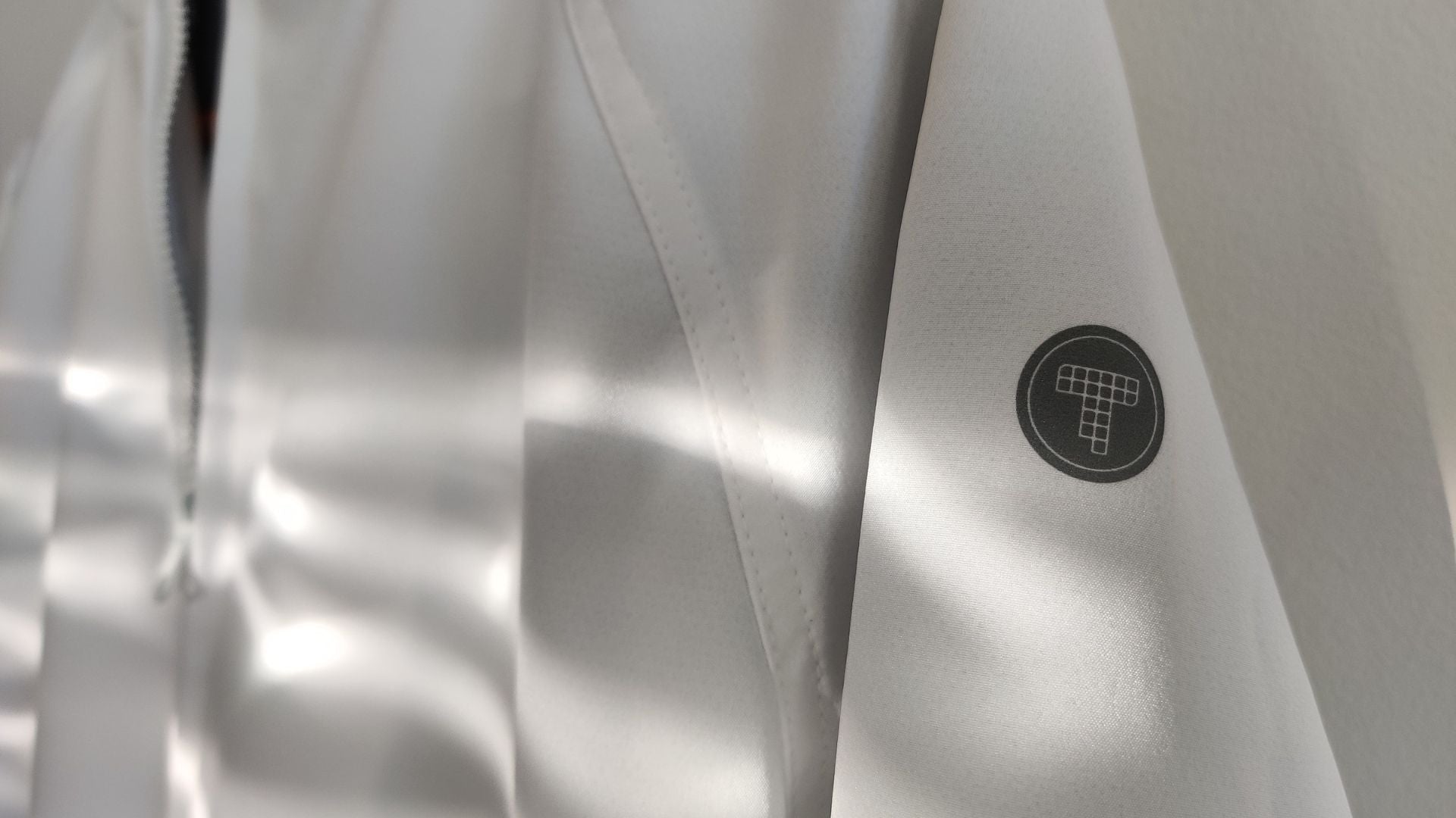 Close up view of the Tingting Athletics brand logo. It is a reflective gray heat transfer logo on a white background. The logo is inspired by the T at the bottom of every lap pool.