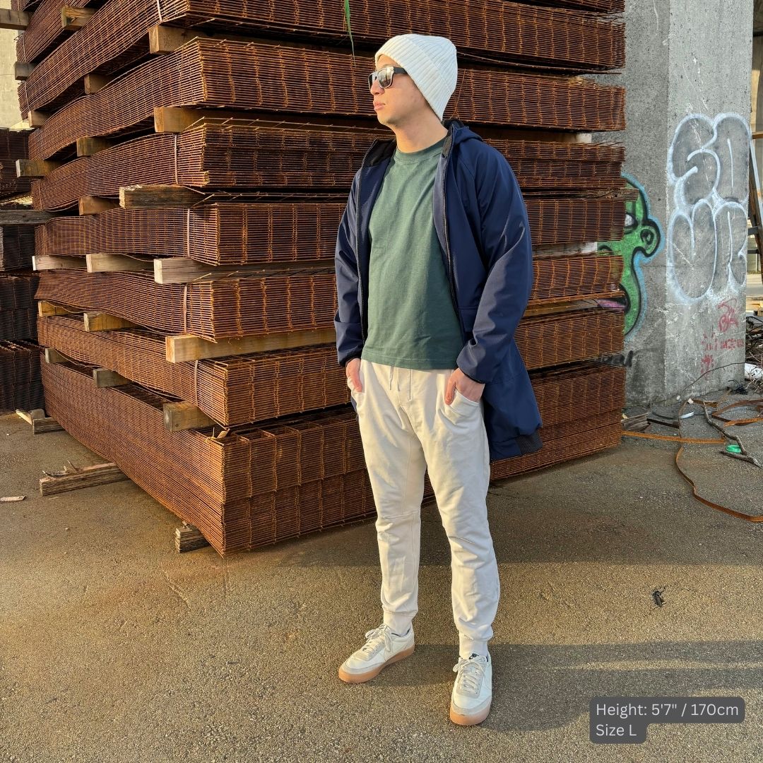 Male model wears navy blue swim parka with a green top, ivory pants, beanie, and sneakers.
